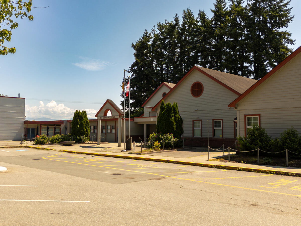 Entrance to an elementary school building. Large green trees in the background and blue sky above.